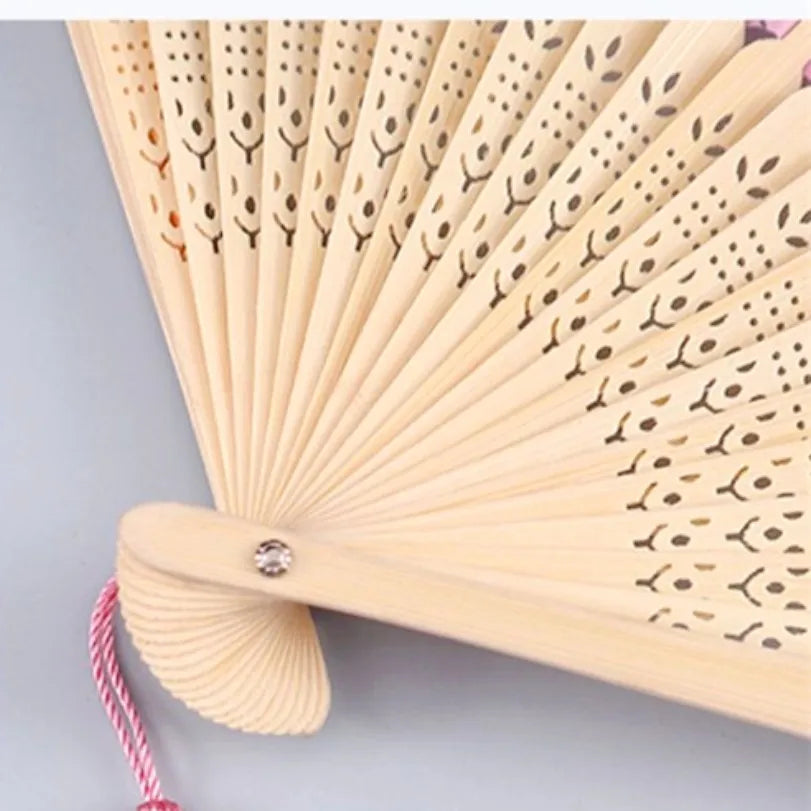 A close-up of a light wood folding hand fan with delicate leaf patterns.