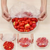 Hands holding a clear reusable food storage bag filled with fresh red tomatoes and apples.