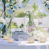 A display of crystal gold votive candle holders and pink and white flowers on a white table.