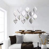 A set of ten reflective acrylic droplet mirror stickers displayed on a white wall above a wooden dining table.