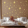 A beige wall decorated with gold star-shaped acrylic mirror stickers, displayed above a white sofa.