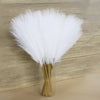 A bundle of white faux pampas grass used as floral decor, displayed in a clear glass vase.