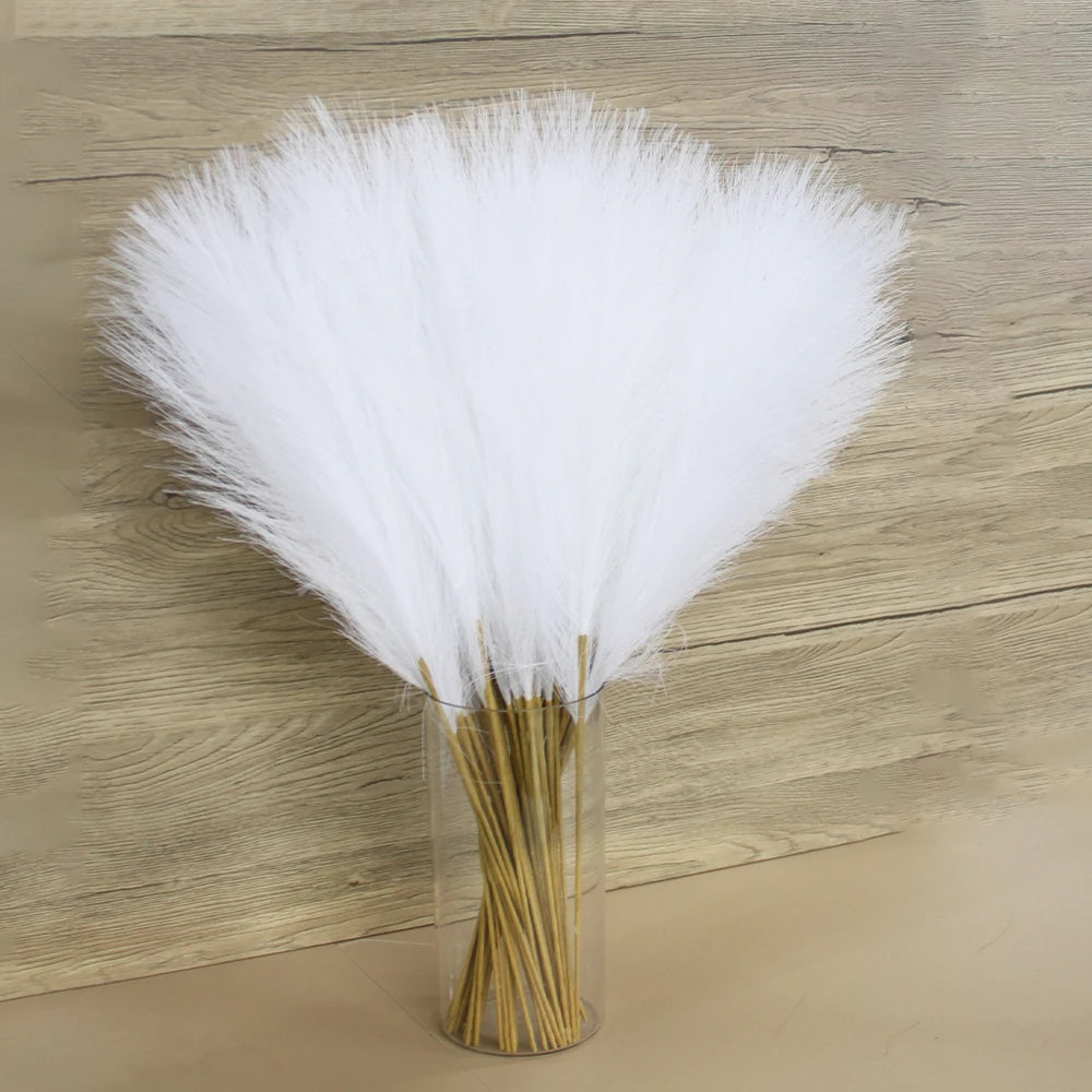 A bundle of white faux pampas grass used as floral decor, displayed in a clear glass vase.