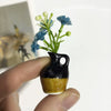 A hand holds a small black ceramic vase with yellow accents and artificial blue flowers.