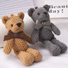 A small, textured brown stuffed bear key pendant with a brown ribbon resting next to a gray stuffed bear.