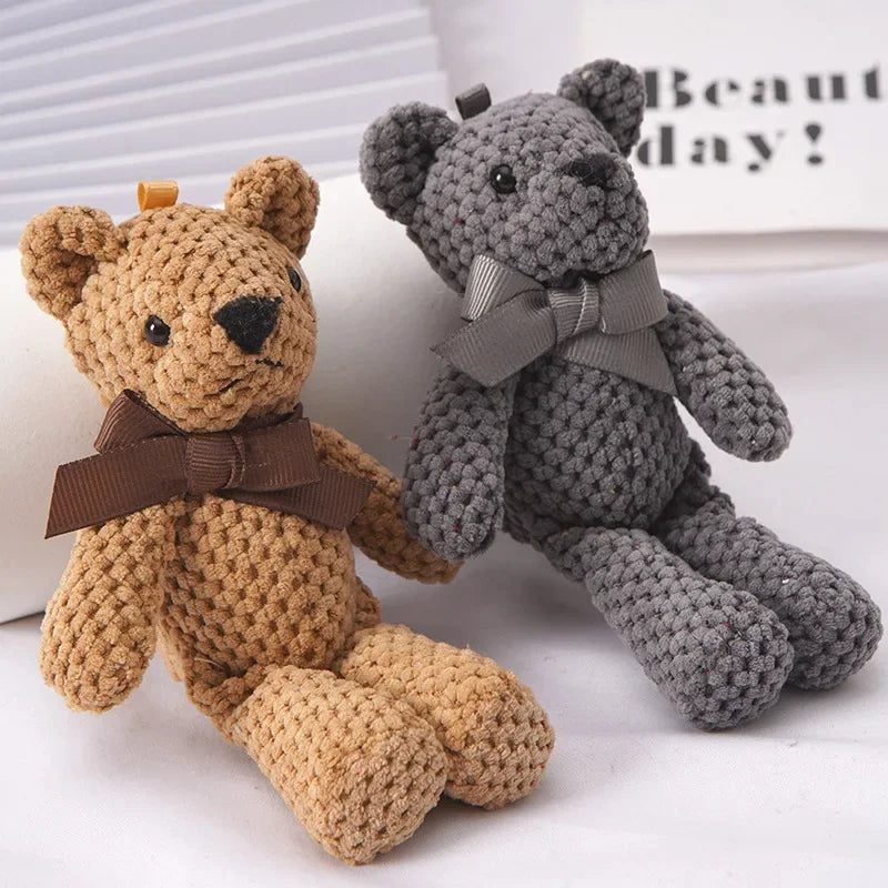 A small, textured brown stuffed bear key pendant with a brown ribbon resting next to a gray stuffed bear.