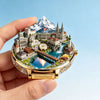A gold-toned watch-shaped fridge magnet featuring an embossed scenic landscape of Switzerland including mountains, architectu