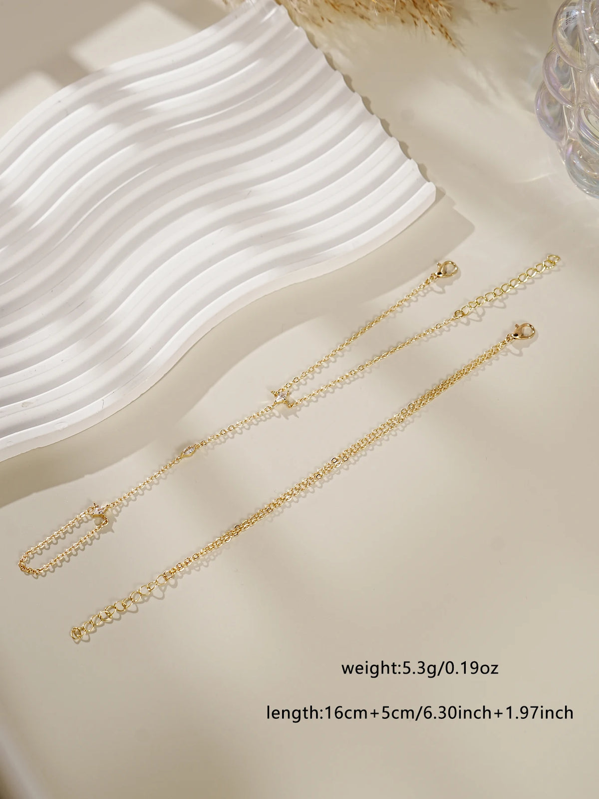 Gold ultra-thin layering chain bracelets displayed on a light background with a white wavy fabric.