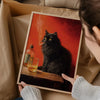 A person holds a framed poster featuring a black cat smoking on a wooden surface.