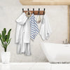 A wooden wall-mounted coat rack with five triple hooks displaying white towels and a bathrobe above a modern sink.