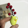 A hand holds a lime green ceramic vase with artificial red flowers, used as a fridge magnet.