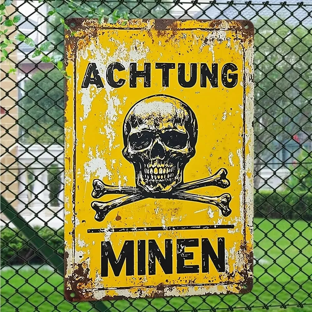 A vintage yellow metal sign with black text warning about mines, displayed outdoors behind a chain-link fence.