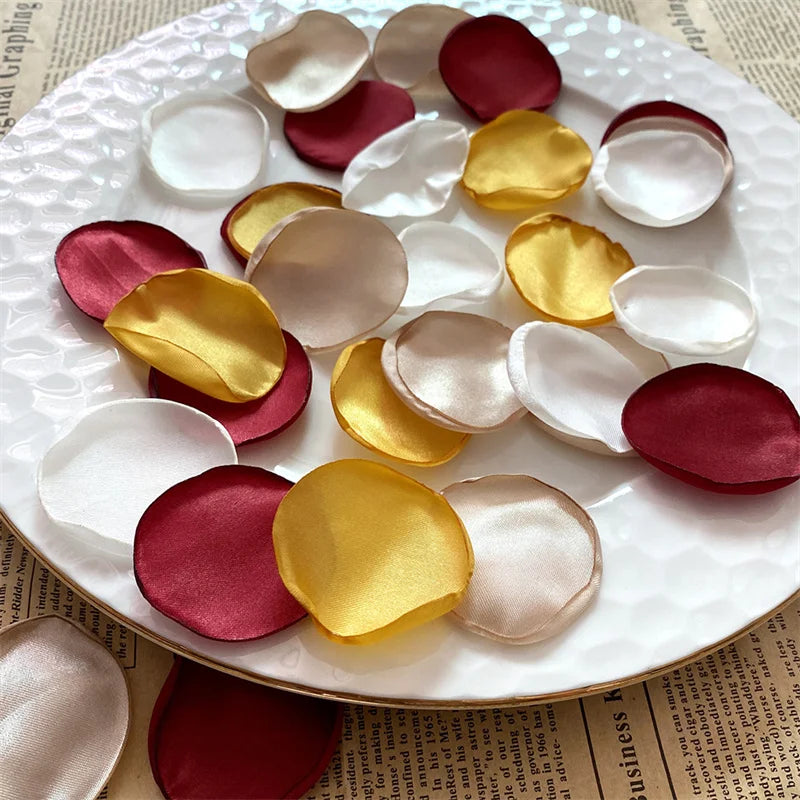 A collection of silk rose petals in shades of pink, red, and gold arranged on a white plate.