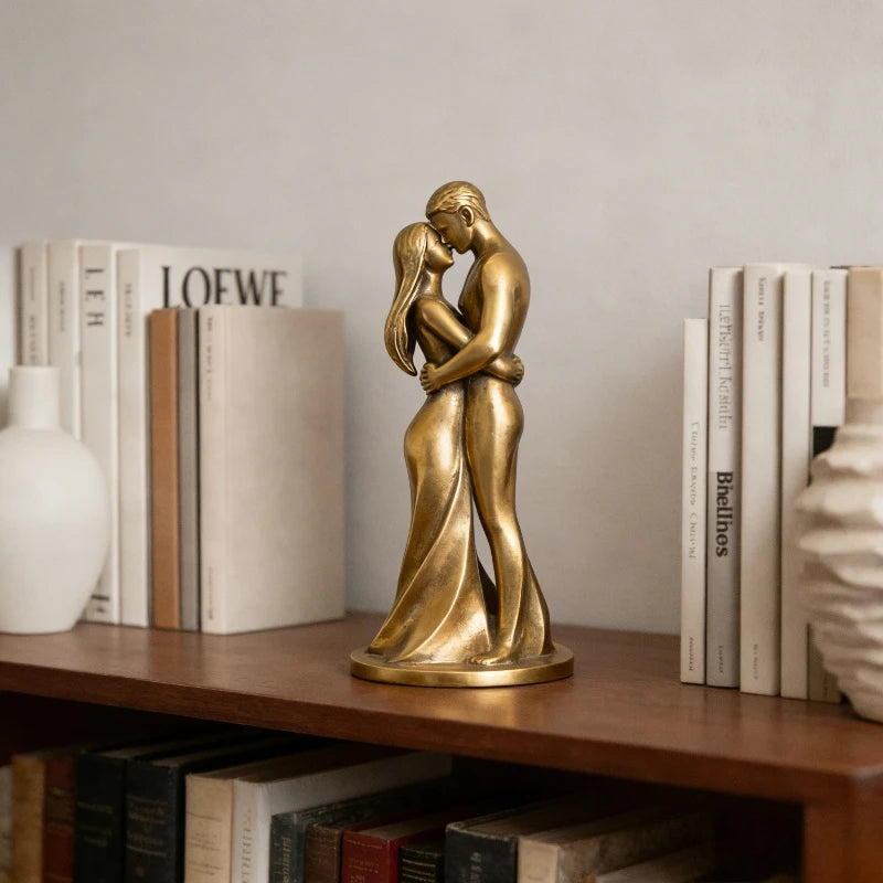 A golden sculpture of a romantic couple hugging, displayed on a wooden shelf among books.