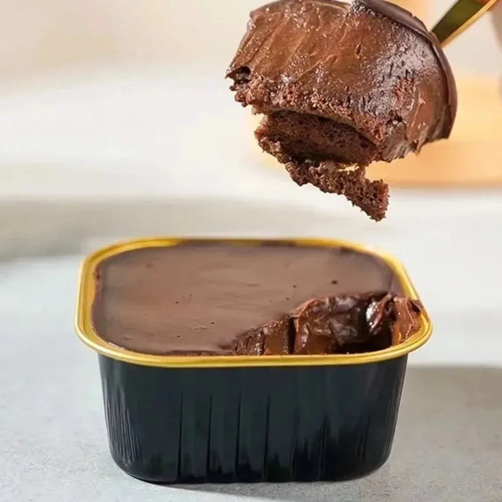 A spoonful of dark chocolate mousse is being lifted from a square aluminum foil baking box.