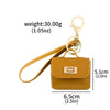 A small mustard yellow leather openable bag attached to a gold-colored keychain.