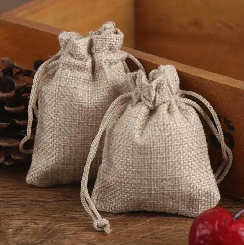Two natural beige burlap drawstring bags resting on a wooden surface.