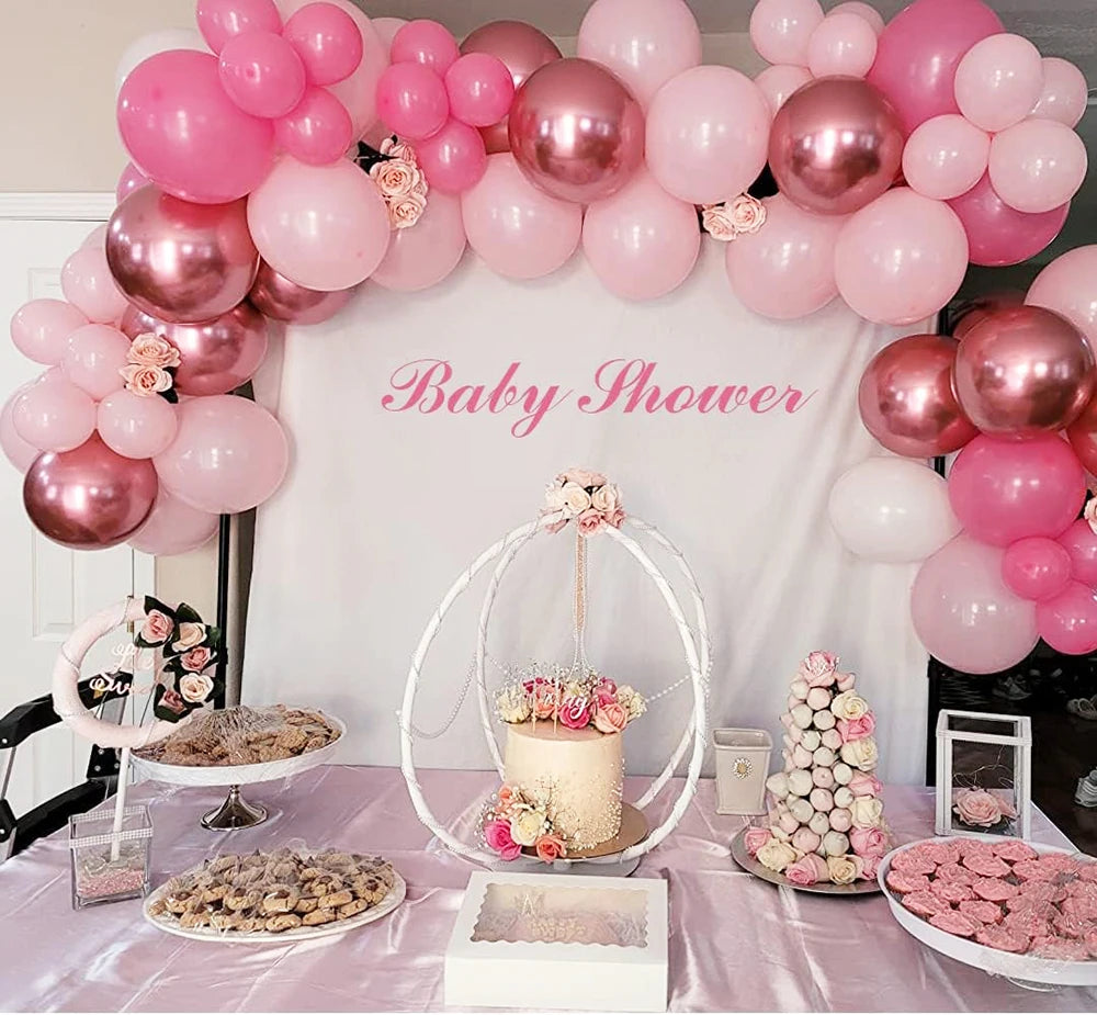 A baby shower setup featuring pink and white latex balloons, confetti, and treats on a table.