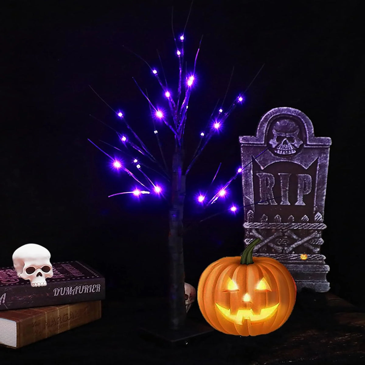 A glowing Halloween birch tree lamp with purple LED lights next to a skull and a carved pumpkin.