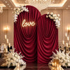 A luxurious red velvet drape backdrop with a glowing love sign and white floral arrangements for an event.