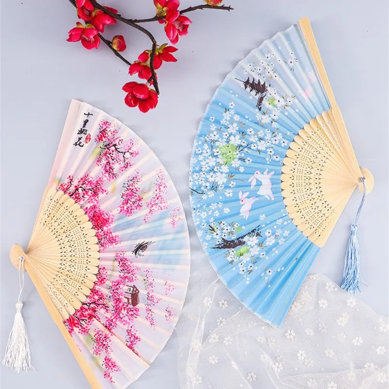 A pair of vintage silk folding hand fans featuring pink cherry blossoms and blue floral patterns.
