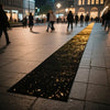 An elegant white sparkling aisle runner laid out on a paved walkway with people walking in the background.