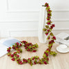 A long garland of deep red roses is displayed in a white vase on a light wooden surface.