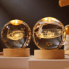 A glass crystal ball night light with a golden glow rests on a wooden base, showing planetary orbits.