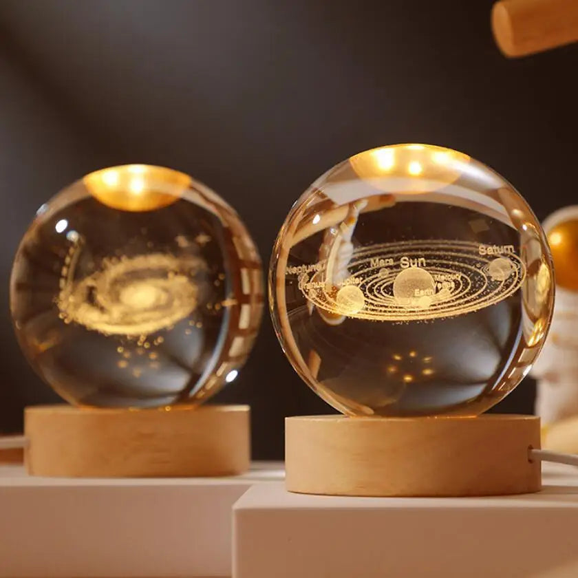 A glass crystal ball night light with a golden glow rests on a wooden base, showing planetary orbits.