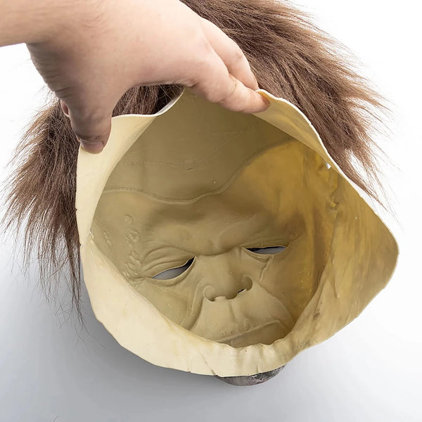 A hand is holding a vintage latex horror mask resembling Michael Myers, showing the facial features and texture.