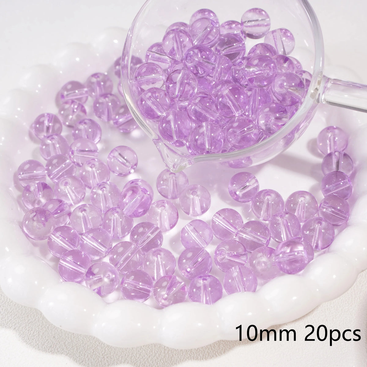 A clear glass container filled with purple round spacer beads for jewelry making resting on a white dish.