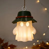 A camping ghost night light hangs, featuring a green hat and a warm glowing face.