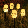 A row of glowing skull solar pathway lights placed in tall grass for Halloween decorations.
