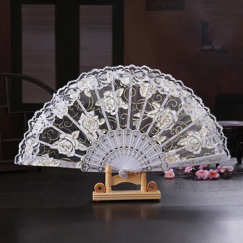 A vintage white lace folding fan decorated with delicate floral patterns, displayed on a wooden stand.
