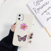 Un smartphone de couleur claire avec un décalcomanie de fleur rose et de papillon à l'arrière, posé sur une surface blanche.