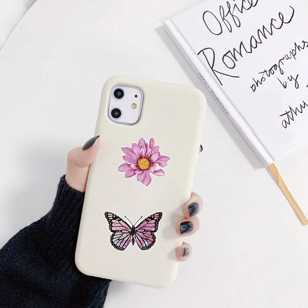 Un smartphone de couleur claire avec un décalcomanie de fleur rose et de papillon à l'arrière, posé sur une surface blanche.