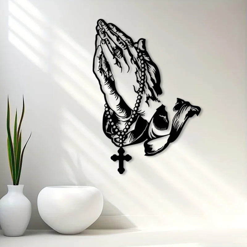 Black metal wall art depicting praying hands with a cross, cast in a silhouette style.