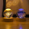 A 3D crystal ball night light with a golden and blue glow rests on a wooden base.