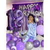 A purple and black birthday balloon set featuring metallic and heart-shaped accents against a purple backdrop.