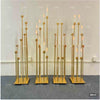 A set of eight gold metal candelabra with tall glass candles displayed against a white wall.