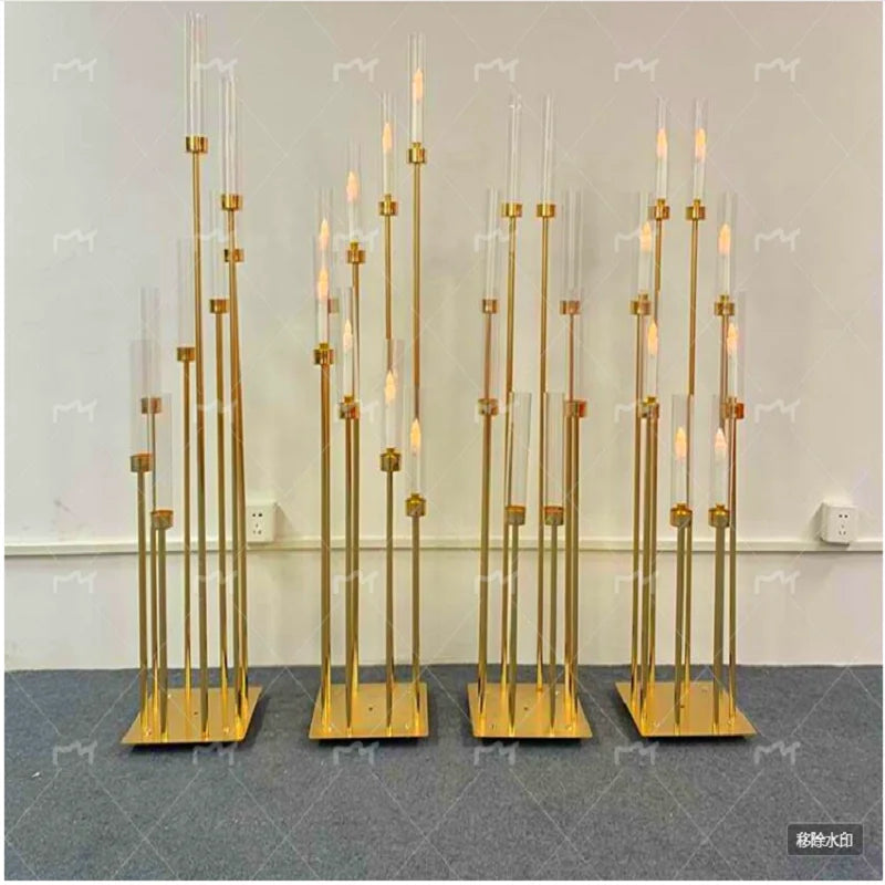 A set of eight gold metal candelabra with tall glass candles displayed against a white wall.
