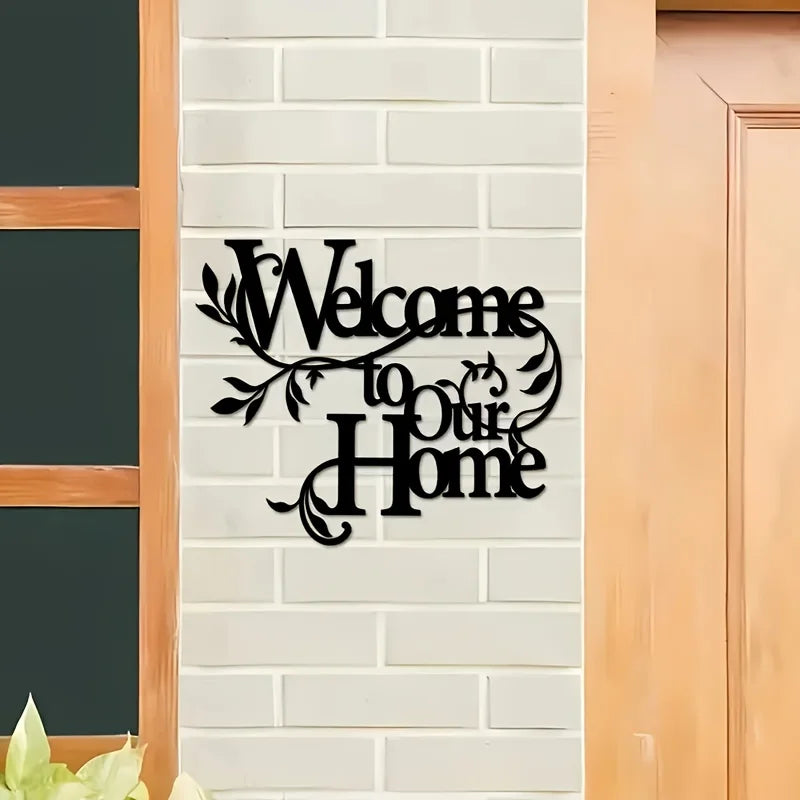 A black metal sign with cursive text welcoming to our home mounted on a white brick wall.