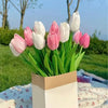 A bouquet of six lifelike artificial tulips in shades of pink and white displayed in a light brown paper sleeve.