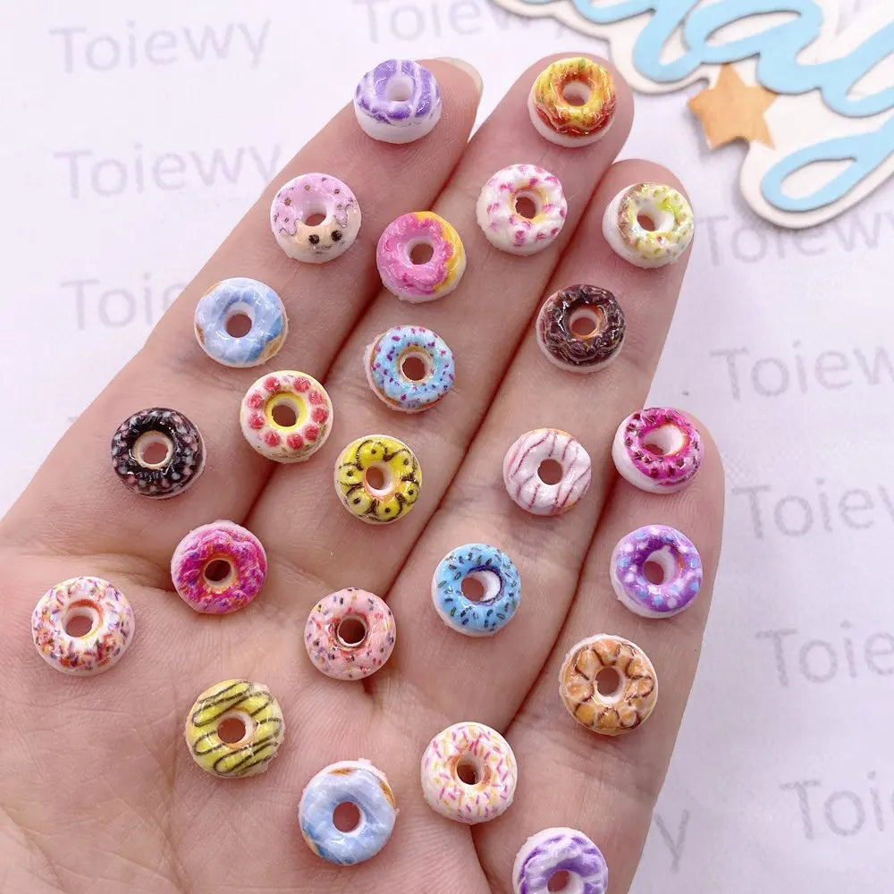 A hand displays a collection of 60 mixed color resin cheese and donut nail art charms on fingernails.
