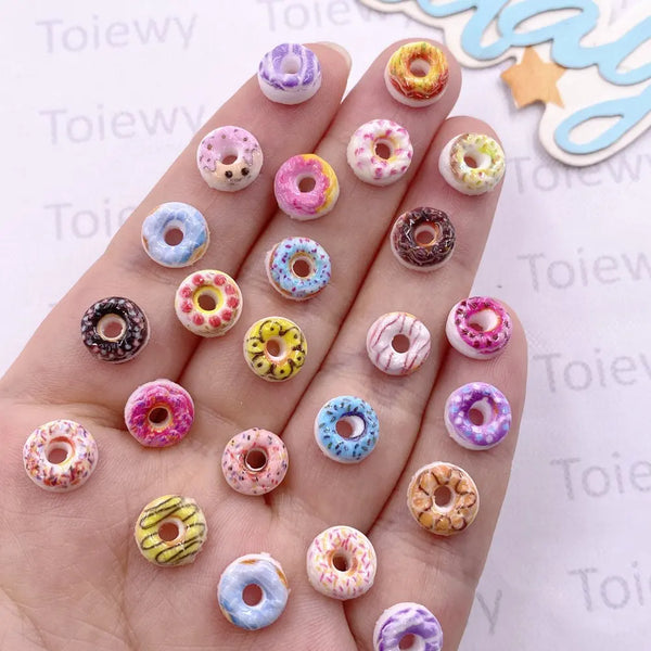 A hand displays a collection of 60 mixed color resin cheese and donut nail art charms on fingernails.