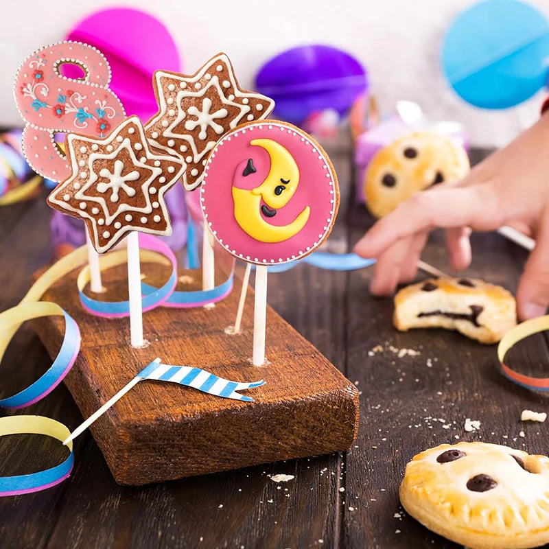 A hand holds a wooden stick with decorated lollipop candy shapes on it, surrounded by colorful spherical candies.