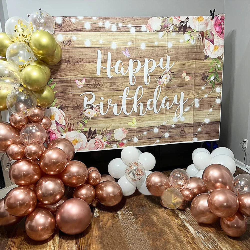 Holzbanner mit Blumen und Lichtern, umgeben von einer großen Anordnung mattrosa und goldener Ballons