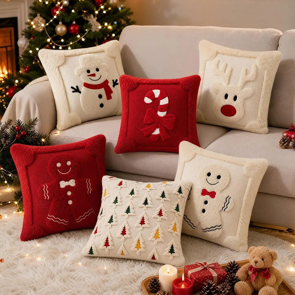 A collection of red and white reindeer and snowman Christmas pillows on a beige sofa with festive greenery.