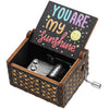 A vintage hand-cranked wooden music box with a lid featuring the text You Are My Sunshine, set in a dark wooden box.