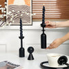 A set of two black decorative candlesticks with fluted columns and a smaller stand, displayed on a white table.